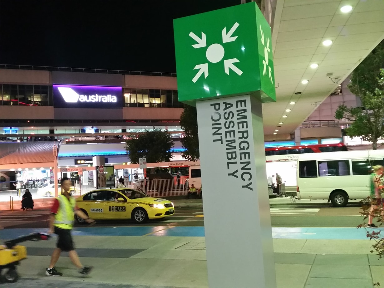 Assembly Point Access Emergency Assembly Point sign on a column outside an airport terminal ...
